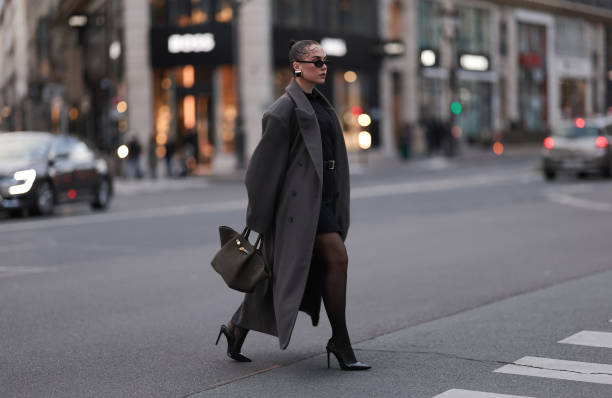 Anna Wein is seen wearing black oval sunglasses; chunky squared earrings in gold with a black stone from H&M Studio; an oversized ankle-length grey...