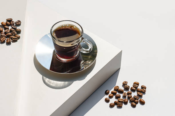 aromatic morning coffee in glass cup and a long shadow from the cup on beige color background. - coffee stock pictures, royalty-free photos & images