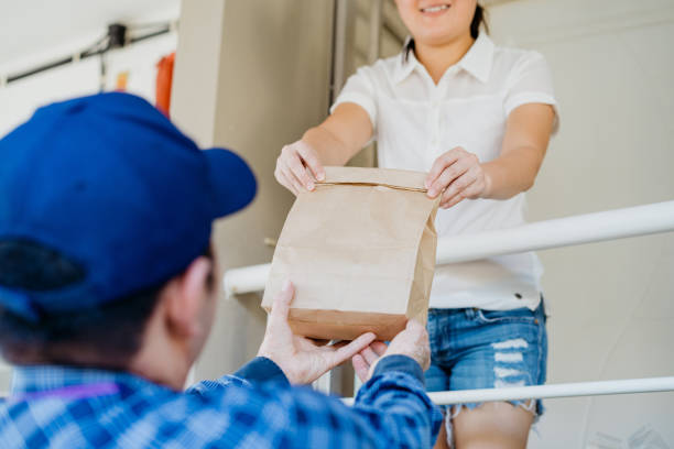 asian chinese woman receiving food delivery from a deliveryman - junk food stock pictures, royalty-free photos & images
