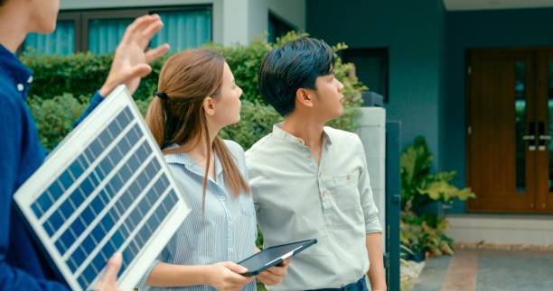 asian real estate agent demonstrates solar panel benefits to interested young couple outside a modern home. consulting eco-friendly home with real estate agent. - home decoration stock pictures, royalty-free photos & images