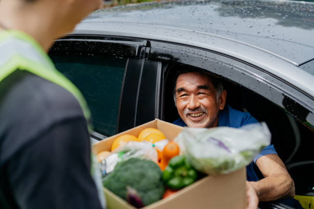 asian senior man receiving donated groceries from volunteer at drive through food bank - food stock pictures, royalty-free photos & images