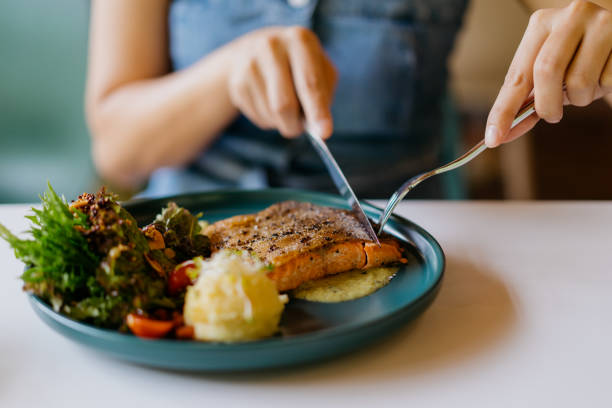 asian woman eating pan fried salmon in cafe - food stock pictures, royalty-free photos & images