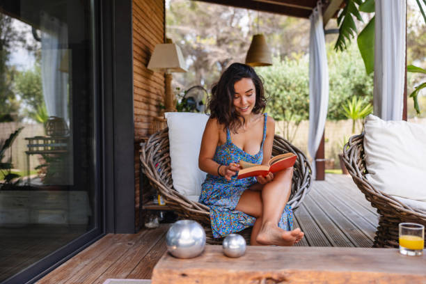 attractive middle eastern woman reading a book on a terrace in the summer - home decoration stock pictures, royalty-free photos & images