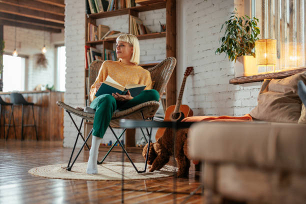 attractive young adult woman reading book in living room. - home decoration stock pictures, royalty-free photos & images
