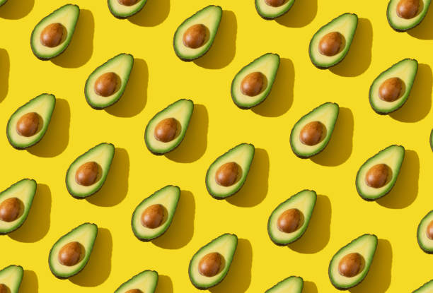 avocado halves pattern with hard shadow and trendy lighting on yellow background - food stock pictures, royalty-free photos & images