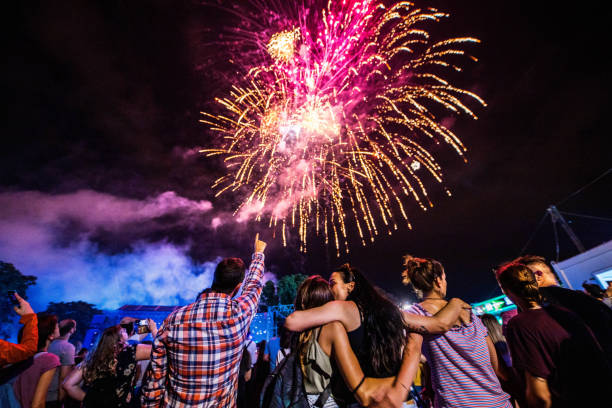 back view of large group of people watching fireworks on the sky by night. - concert stock pictures, royalty-free photos & images