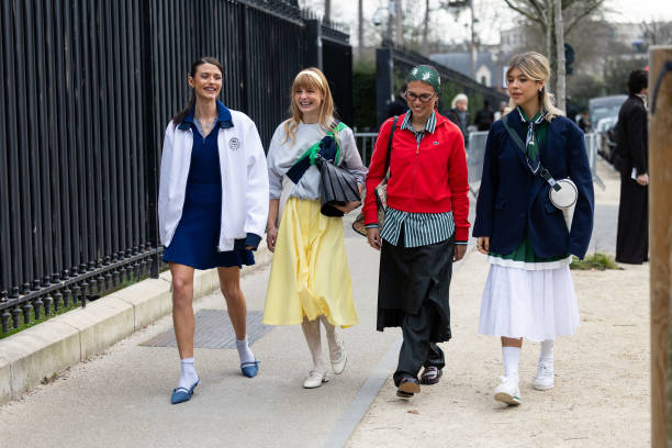 Barbara Ines wears a white jacket, a blue mini polo dress, white socks, blue heeled slingback and a white leather bag, in the middle a guest wears a...