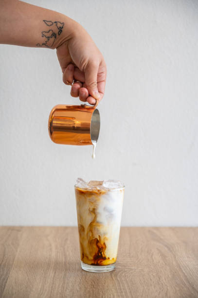 barista hand pouring milk into an iced coffee for making iced latte. - coffee stockfoto's en -beelden