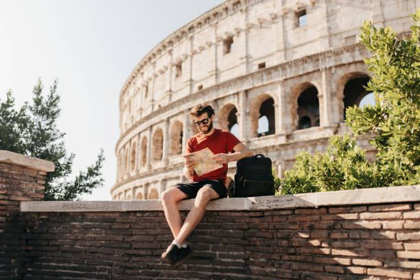 bearded male tourist reading map and smiling with colosseum in background - travel stock pictures, royalty-free photos & images