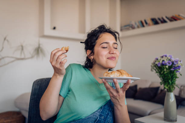 beautiful girl enjoying the taste of a fresh croissant - junk food stock pictures, royalty-free photos & images