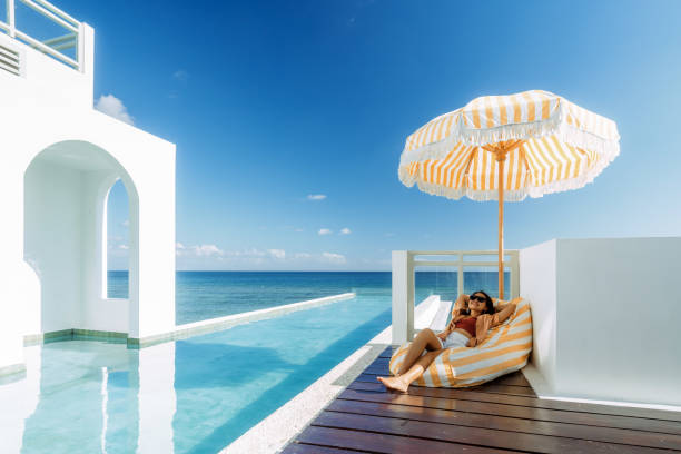 beautiful indonesian relaxing under yellow stripped umbrella at the infinity pool side - travel stock pictures, royalty-free photos & images