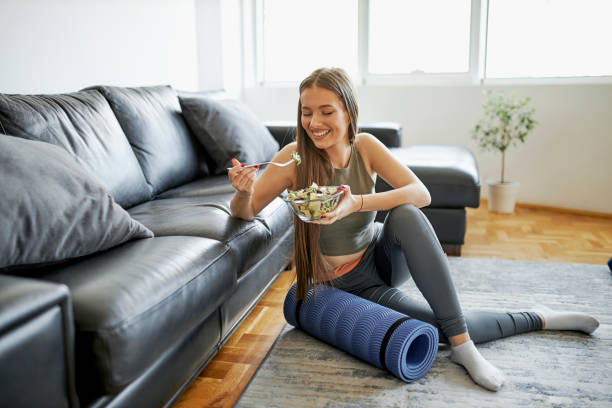 beautiful woman eating fresh salad after intensive home workout - food stock pictures, royalty-free photos & images