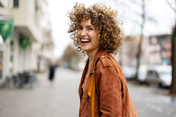 beautiful woman walking outdoors looking behind and laughing - fashion stock pictures, royalty-free photos & images