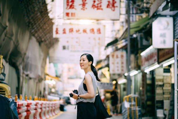 beautiful young woman carrying camera exploring and walking through local city street - travel stock pictures, royalty-free photos & images