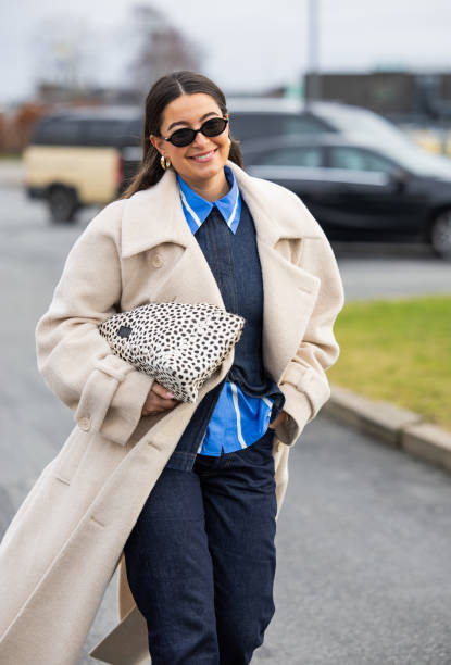 Benthe Liem wears beige coat, dark denim jeans, denim shirt, bag with dots print outside Marimekko during the Copenhagen Fashion Week Autumn/Winter...