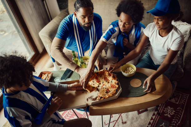 black family of soccer fans having pizza for lunch at home. - junk food stock pictures, royalty-free photos & images