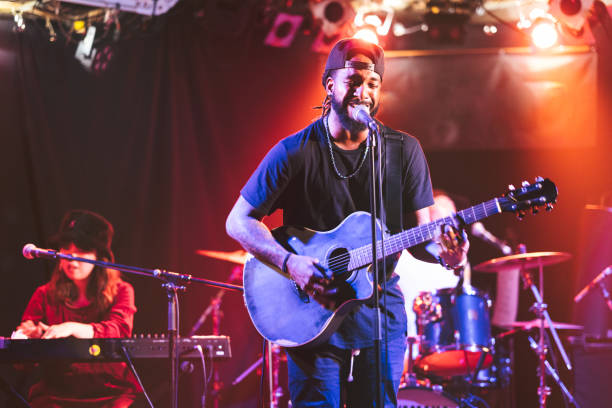 black male guitarist singing and playing acoustic guitar on stage - concert stock pictures, royalty-free photos & images