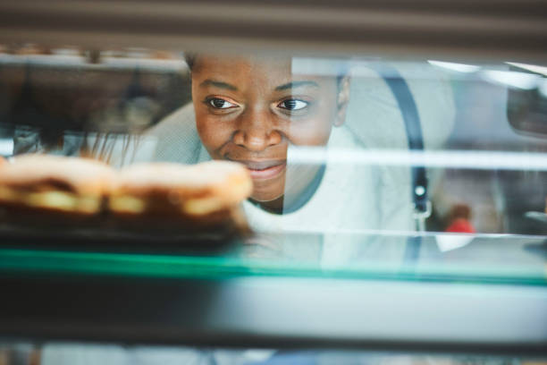 black woman, bakery customer and glass for dessert, cake or sweet food from retail, store or grocery shop. woman, happy and shopping in supermarket, mall or cafe for discount, sale or deal with smile - junk food stock picture