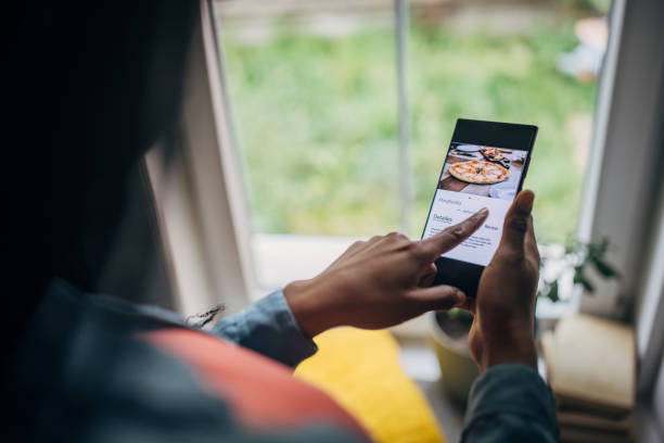 black woman in her home, ordering food online through a mobile app on her phone - food stock pictures, royalty-free photos & images