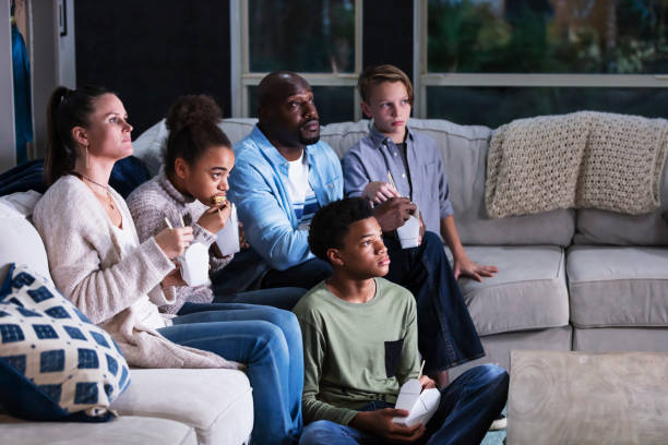 blended family of five watching tv, eating takeout - junk food stock pictures, royalty-free photos & images