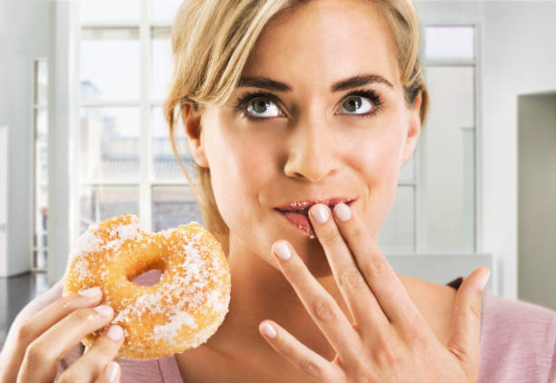 blonde woman eating a sugar coated doughnut - junk food stock pictures, royalty-free photos & images