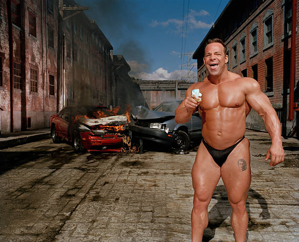 bodybuilder eating ice cream cone, car collision in background - food stockfoto's en -beelden