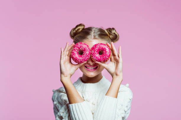 bonita chica adolescente sosteniendo donuts rosas, retrato sobre fondo rosa - food fotografías e imágenes de stock