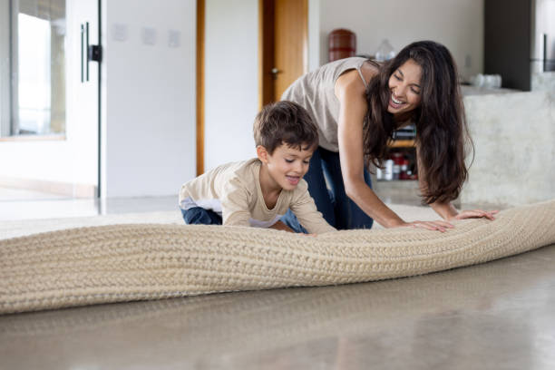 boy helping his mother unroll a carpet at home - home decoration stock pictures, royalty-free photos & images