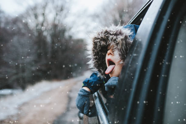 boy on a road trip. the little boy is looking from the car window in winter , opened his mouth and pulled out his tongue, catches snowflakes - travel stock pictures, royalty-free photos & images