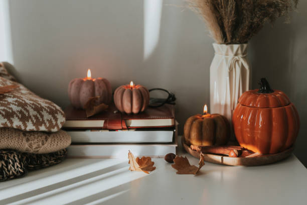 burning candles shape of pumpkin, stack knitted season sweaters, daily and autumn leaves. cozy autumn lifestyle, hygge concept. still life - home decoration stock pictures, royalty-free photos & images