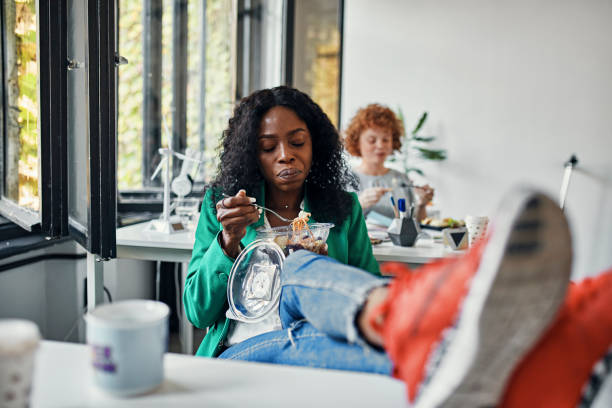 businesswoman having lunch break in office with feet on desk - junk food stock pictures, royalty-free photos & images