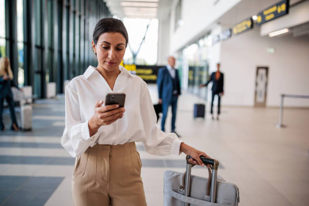 businesswoman using a smartphone in an airport terminal - travel stock pictures, royalty-free photos & images