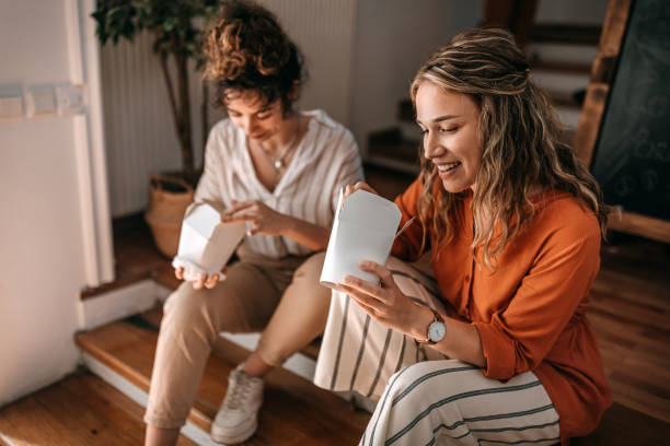 businesswomen eating food sitting on stairs during lunch break at office - junk food stock pictures, royalty-free photos & images