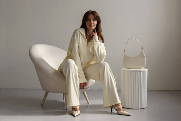 calm confident young woman sitting in chair looking at camera in fashionable clothes. clothing sale concept. - fashion stock pictures, royalty-free photos & images