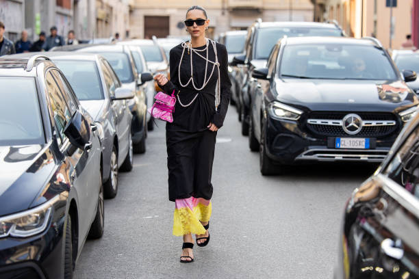 Candela Pelizza wears pink bag, black dress, pearl necklace outside Moschino during the Milan Fashion Week Womenswear Fall/Winter 2025/2026 on...