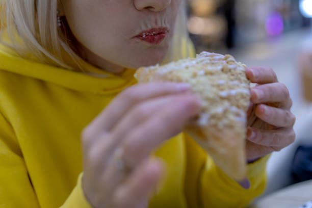captured in exquisite detail, this photo showcases a woman's delightful bite into a cozy bun. the pastry's golden brown exterior contrasts beautifully with her softly glossed lips - junk food stock pictures, royalty-free phot