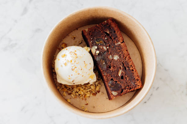 cardboard box of delicious fresh brownie and vanilla ice cream with nuts and citrus crumb on marble table. takeaway food - junk food stock pictures, royalty-free photos & images