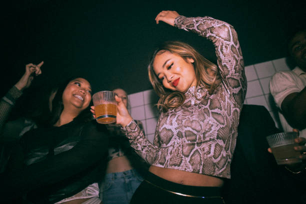 carefree young woman with drink dancing by female friend enjoying at nightclub - concert stock pictures, royalty-free photos & images