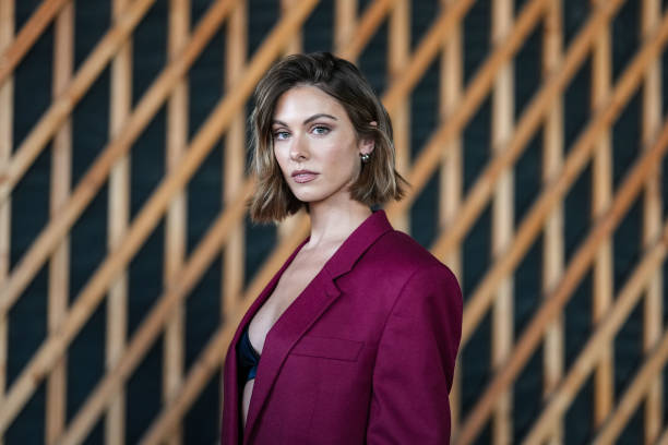 Carmella Rose wears light brown wavy short hair, black bralette, burgundy bordeaux oversized blazer jacket, outside Stella McCartney, during the...