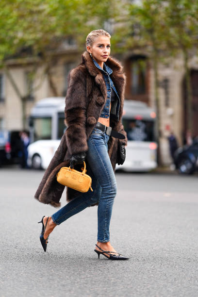 Caroline Daur wears silver earrings, black bandeau top, navy blue denim jean cropped jacket, black belt, washed navy blue denim jean skinny pants,...