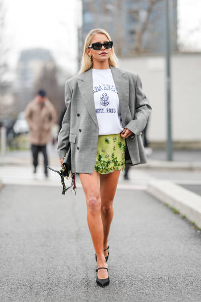 Caroline Daur wears silver earrings, white Prada purple t-shirt, light green floral beaded detail Prada mini skirt, black leather bag, light gray...