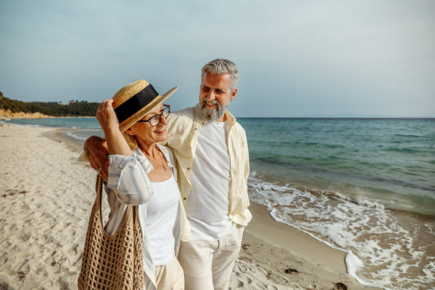 casually clothed mature couple enjoying walk by the sea together - travel stock pictures, royalty-free photos & images
