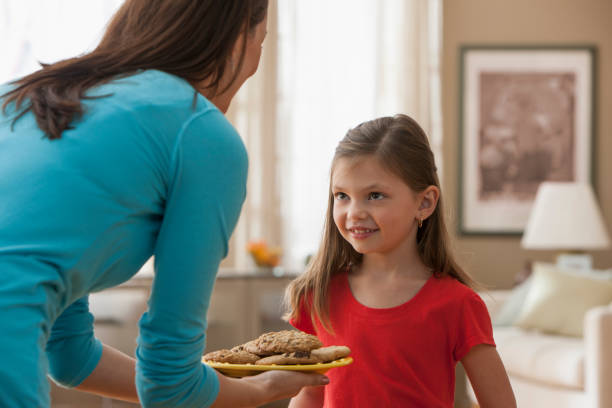 caucasian mother offering daughter cookies - junk food stock pictures, royalty-free photos & images