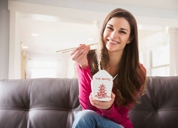 caucasian woman eating chinese food on sofa - junk food stock pictures, royalty-free photos & images