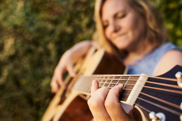 caucasian woman playing acoustic guitar in the garden. musical concept. - concert stock pictures, royalty-free photos & images