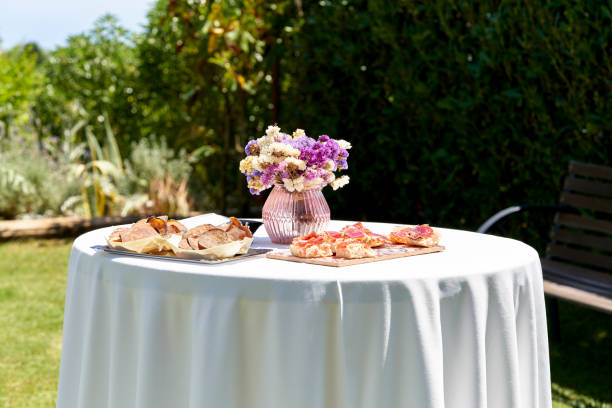 celebrating spring in the garden, decorated by a round table with a white tablecloth, a beautiful crystal vase with multicolored flowers, trays with appetizers and pizzas ready to be savored. - garden decoration stock picture