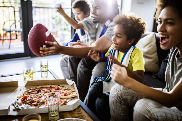cheerful black family cheering while watching rugby match on tv at home. - junk food stock pictures, royalty-free photos & images