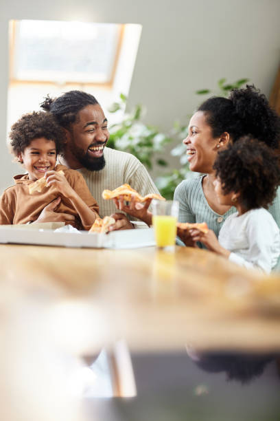 cheerful black family talking while eating pizza for lunch in dining room. - junk food stock pictures, royalty-free photos & images