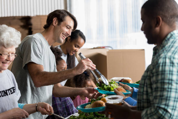 cheerful caucasian man serves healthy meal in soup kitchen - food stock pictures, royalty-free photos & images