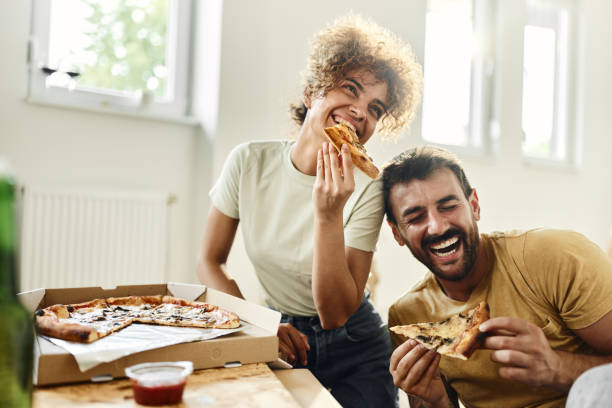 cheerful couple eating pizza on a break from home renovation process. - junk food stock pictures, royalty-free photos & images